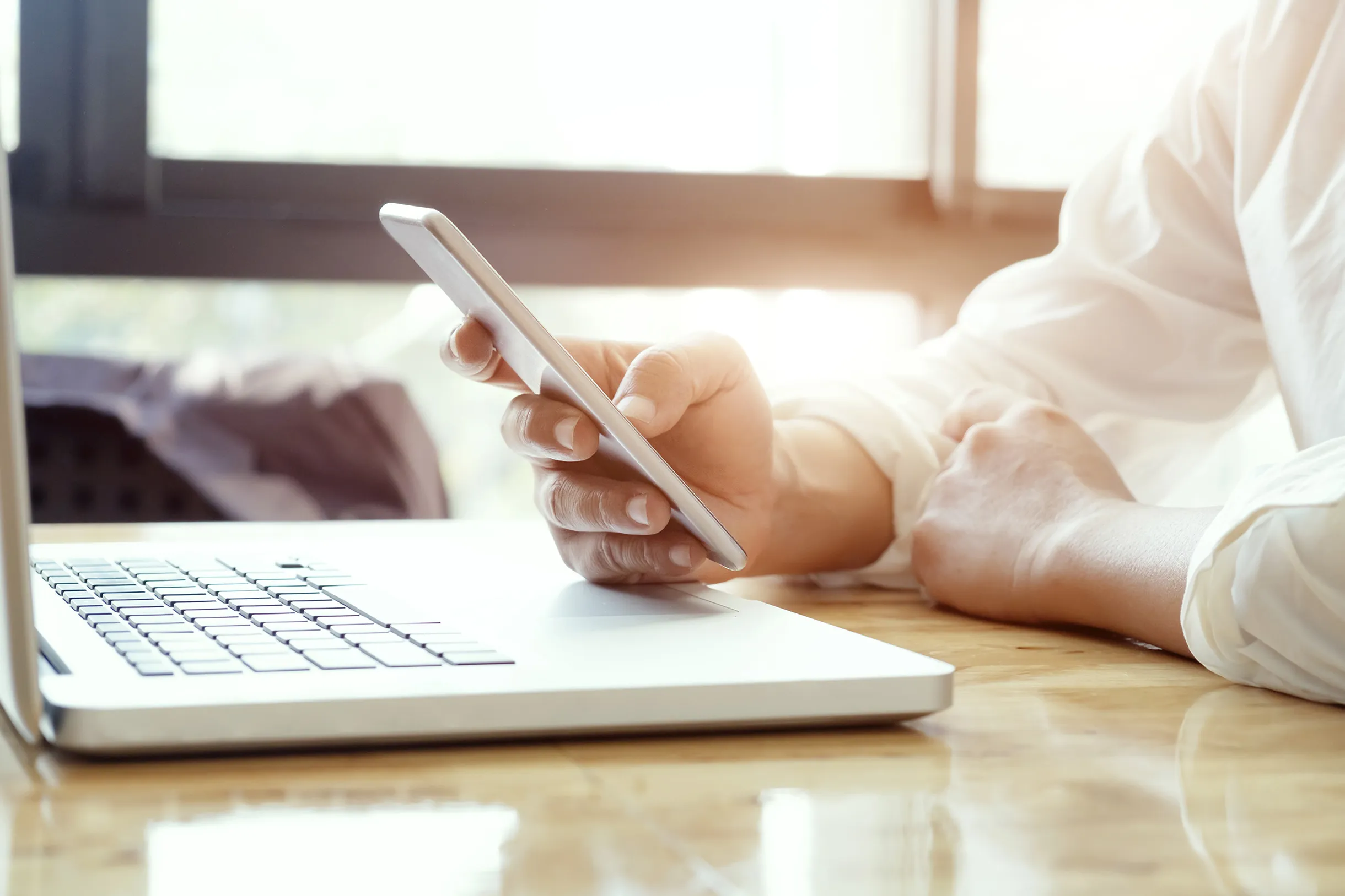 Un homme utilisant son smartphone face à son ordinateur portable